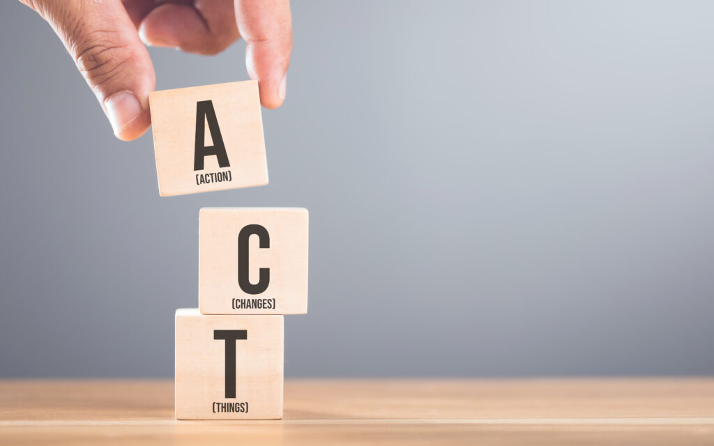 Hand arranging wooden blocks with the letters A, C and T on a table, set against a gray. Symbolizes the process of taking action to implement changes in various aspects of life or business
