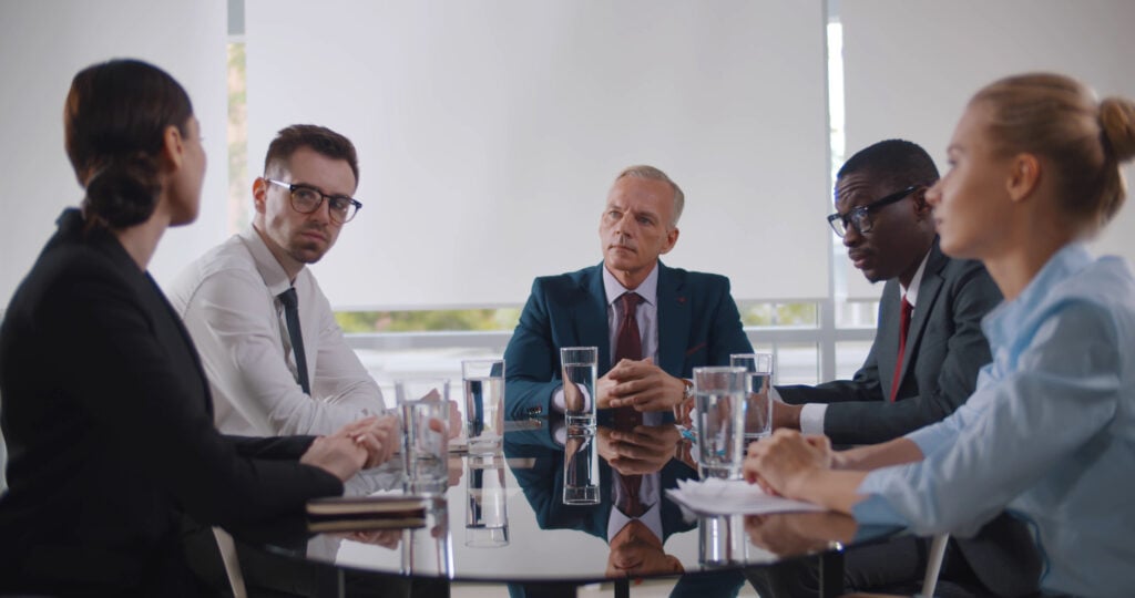 Business leader holding corporate meeting with team in boardroom. Multiracial business partners at meeting in conference room sitting at desk and discussing contract